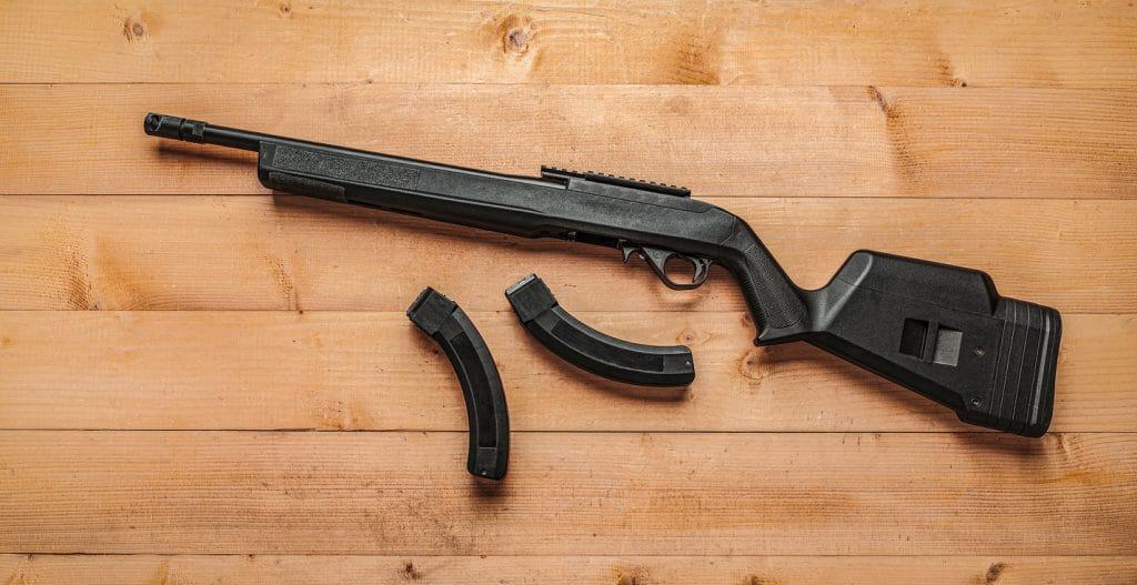 Modern semi-automatic small-caliber .22lr rifle on a light wooden background. Sports carabiner .22lr and several clips to it on a wooden table.