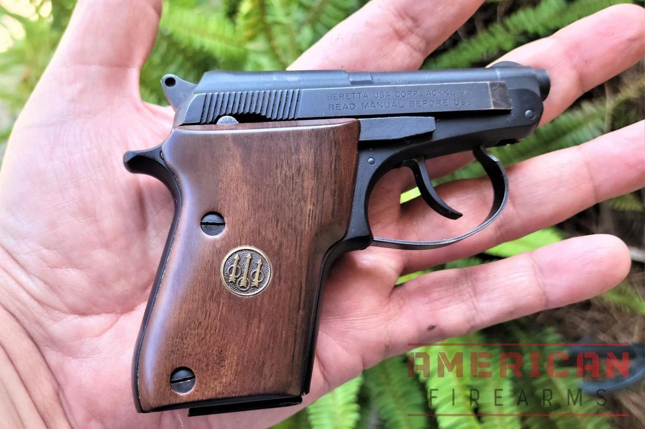 A close-up of a Beretta Bobcat pistol in hand. The pistol is small and black, with a textured walnut grip.