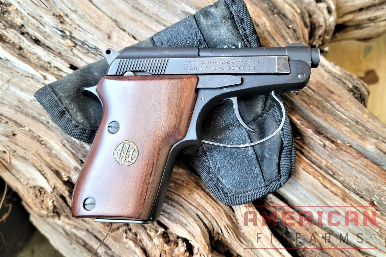 A Beretta Bobcat pistol rests on a black pocket holster and weathered wooden log.